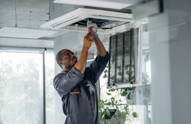 high up, fixing the ventilation. repairman is indoors in the modern office.